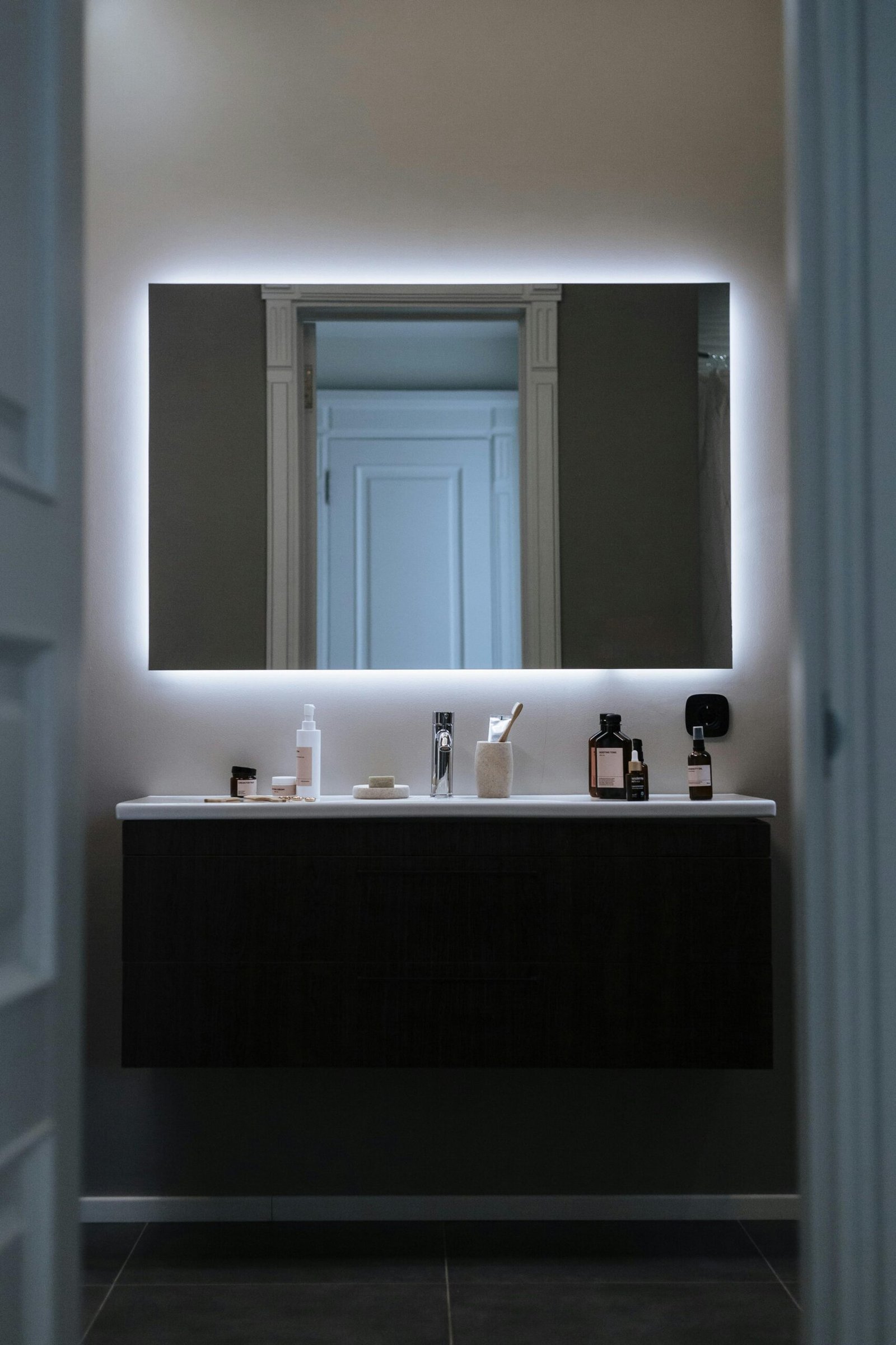 Contemporary bathroom featuring a sleek design with LED mirror and cosmetic products.