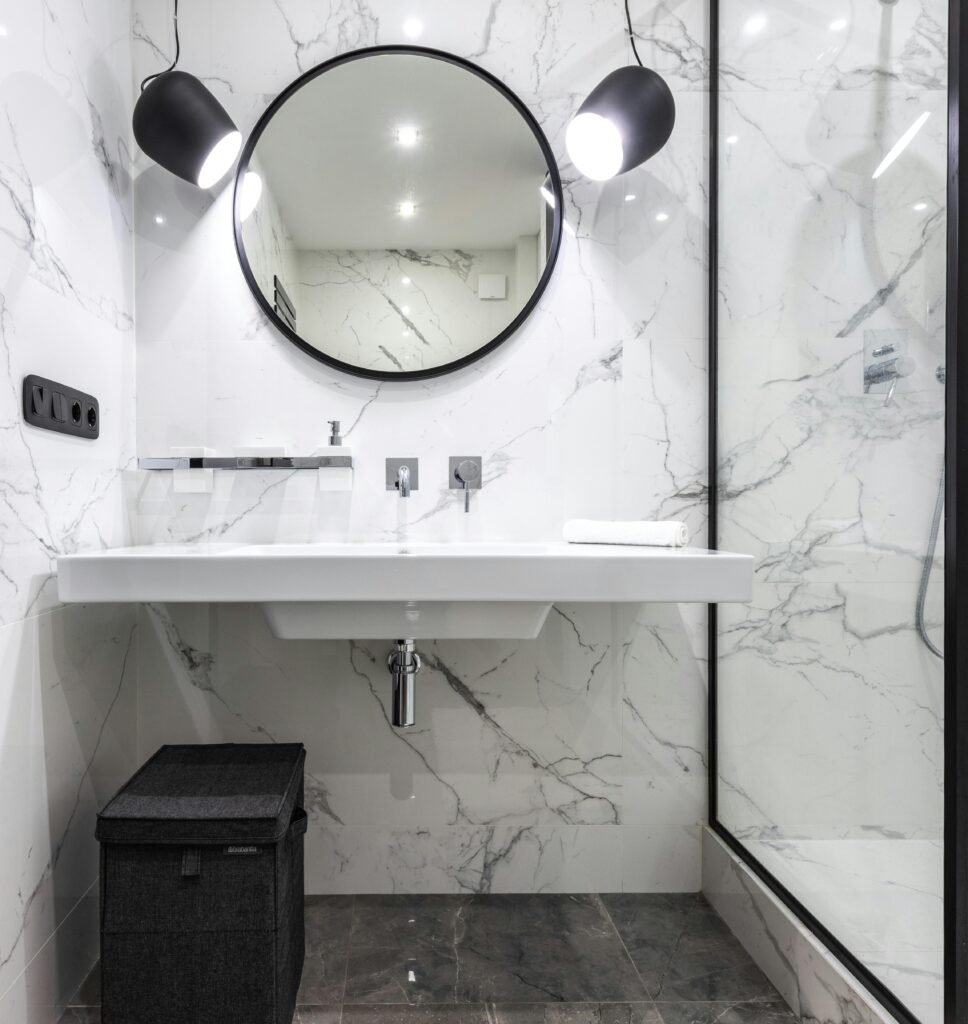 Elegant bathroom with marble walls, round mirror, and contemporary lighting.